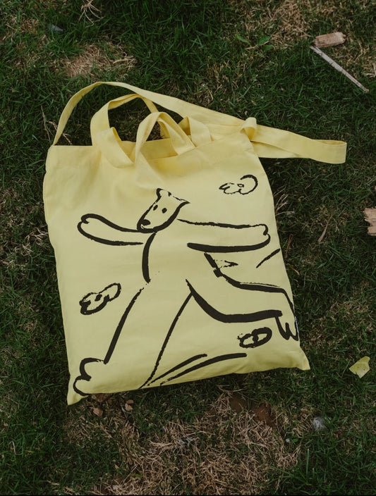 A person wearing a capsule wardrobe outfit carrying a natural fabric bag while walking in a sunny park.