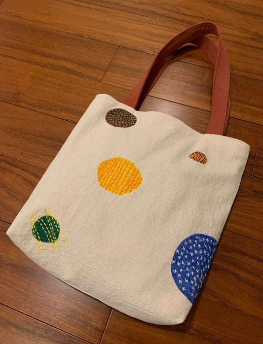 A hand-painted canvas tote bag showing the texture of eco-friendly ink and manual embroidery.
