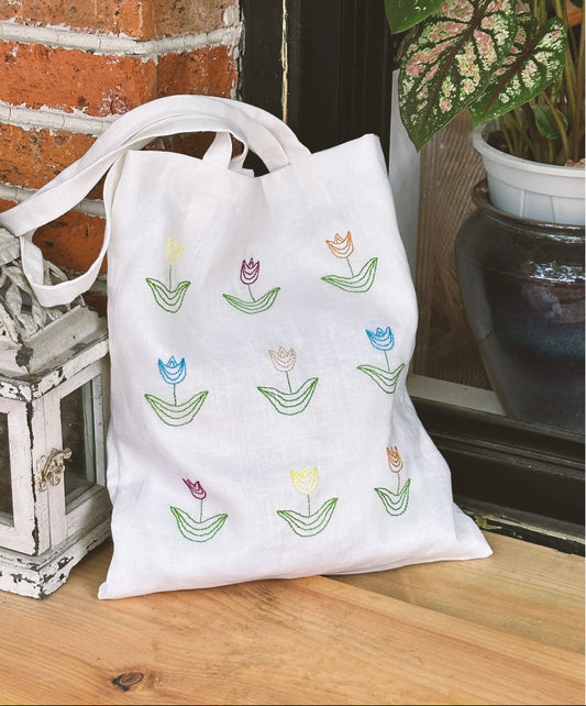 Close-up of a hand-embroidered floral cotton tote bag with intricate needlework details.