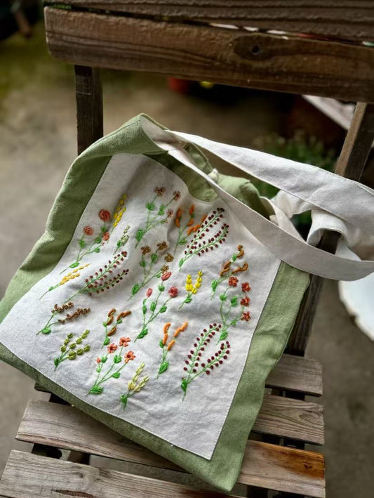 A person carrying a personalized embroidered tote bag filled with books and a laptop on a city street.