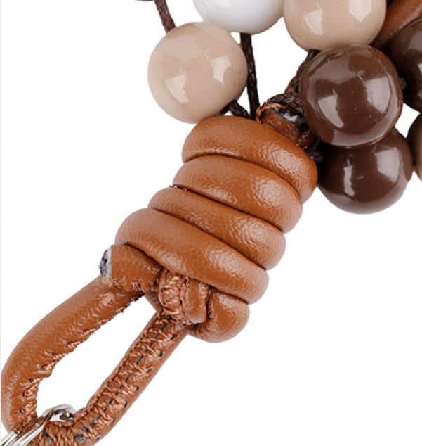Minimalist beaded phone strap accessory hanging against a neutral textured background
