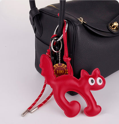 White cat bag charm with woven cord accent clipped to a beige shoulder bag