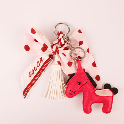 Pink bow keychain hanging from a bag strap