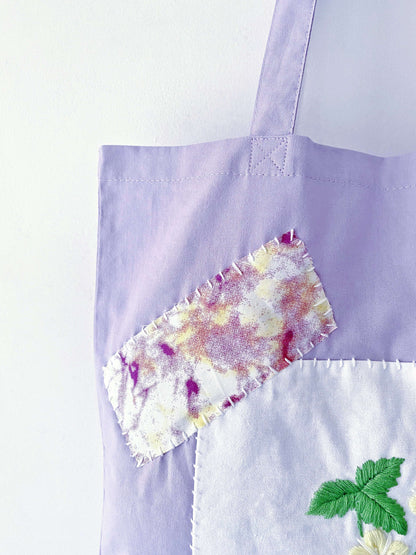 Hand touching textured floral embroidery on bag, emphasizing the grounding tactile comfort of handmade goods.
