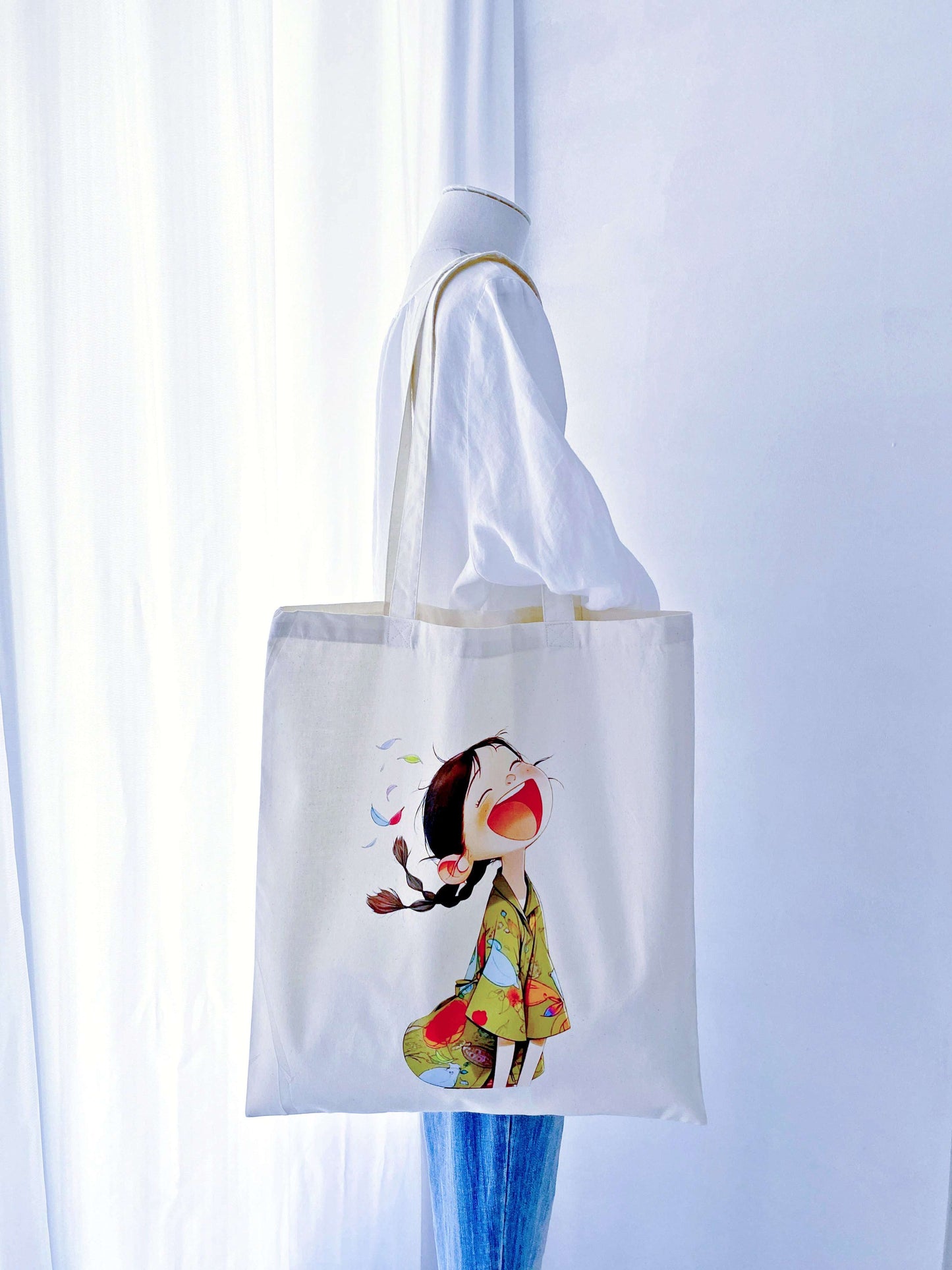 A joyful, hand-printed 'laughing girl' design on this cotton tote, offering a bright and sustainable gift option for loved ones.