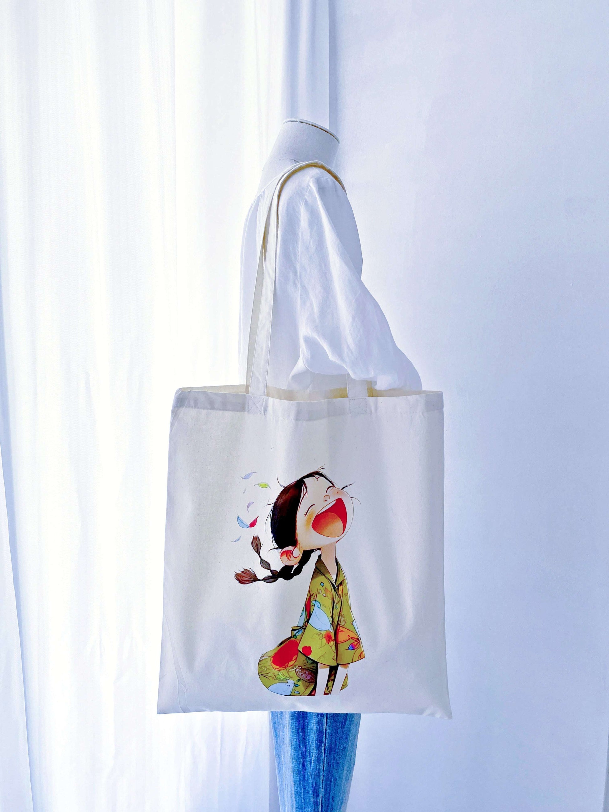 A joyful, hand-printed 'laughing girl' design on this cotton tote, offering a bright and sustainable gift option for loved ones.