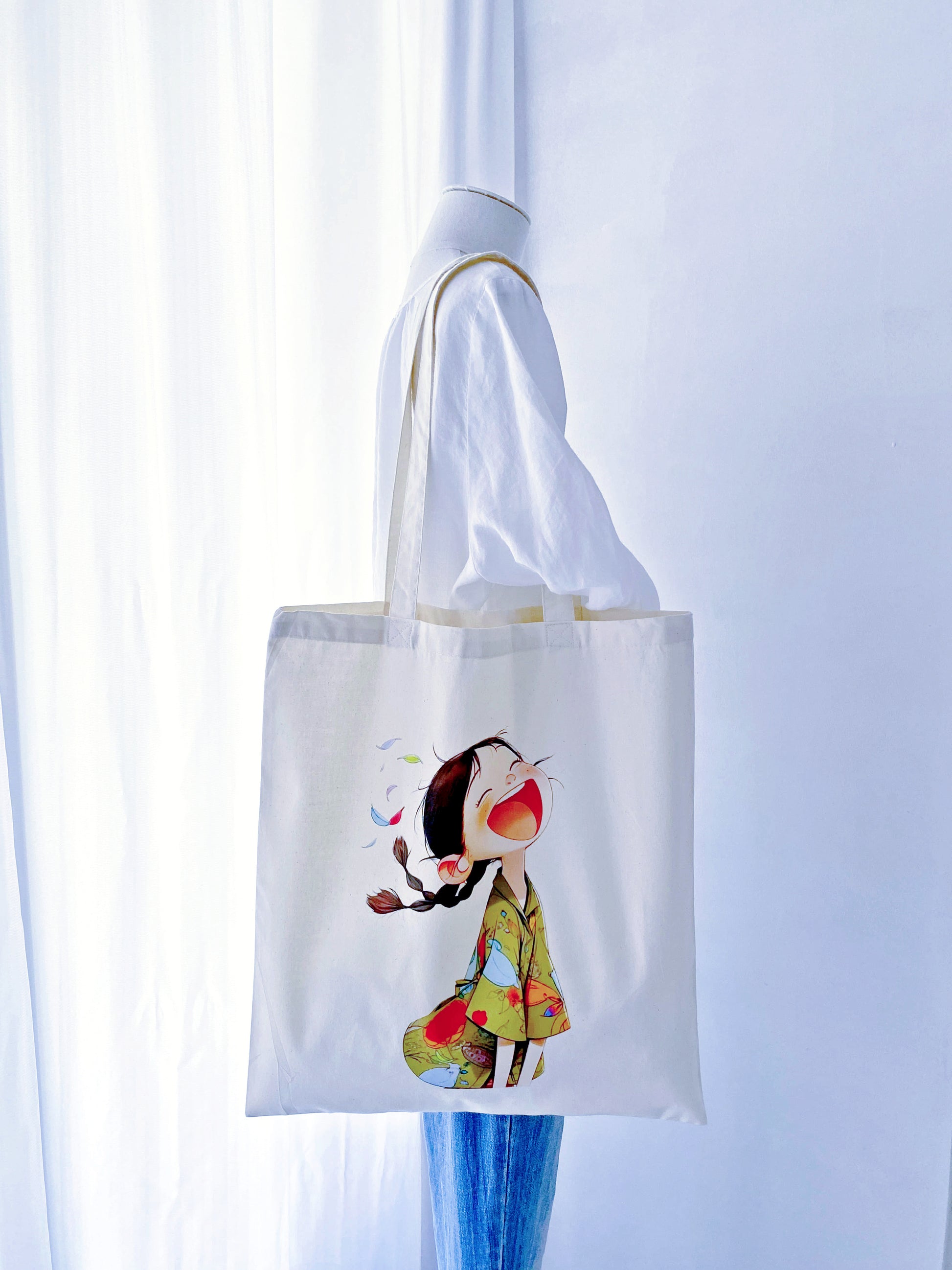 A joyful, hand-printed 'laughing girl' design on this cotton tote, offering a bright and sustainable gift option for loved ones.
